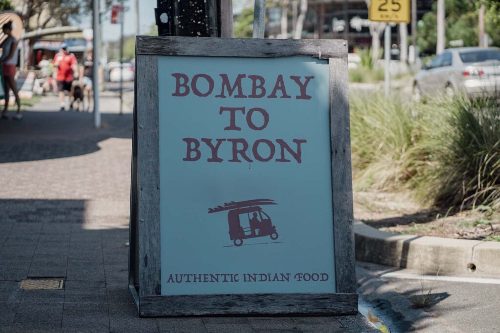 An A frame sign board featuring Bombay to Byron. A modern Indian restaurant nestled in the heart of Byron Bay, available for dine in, takeaway or delivery